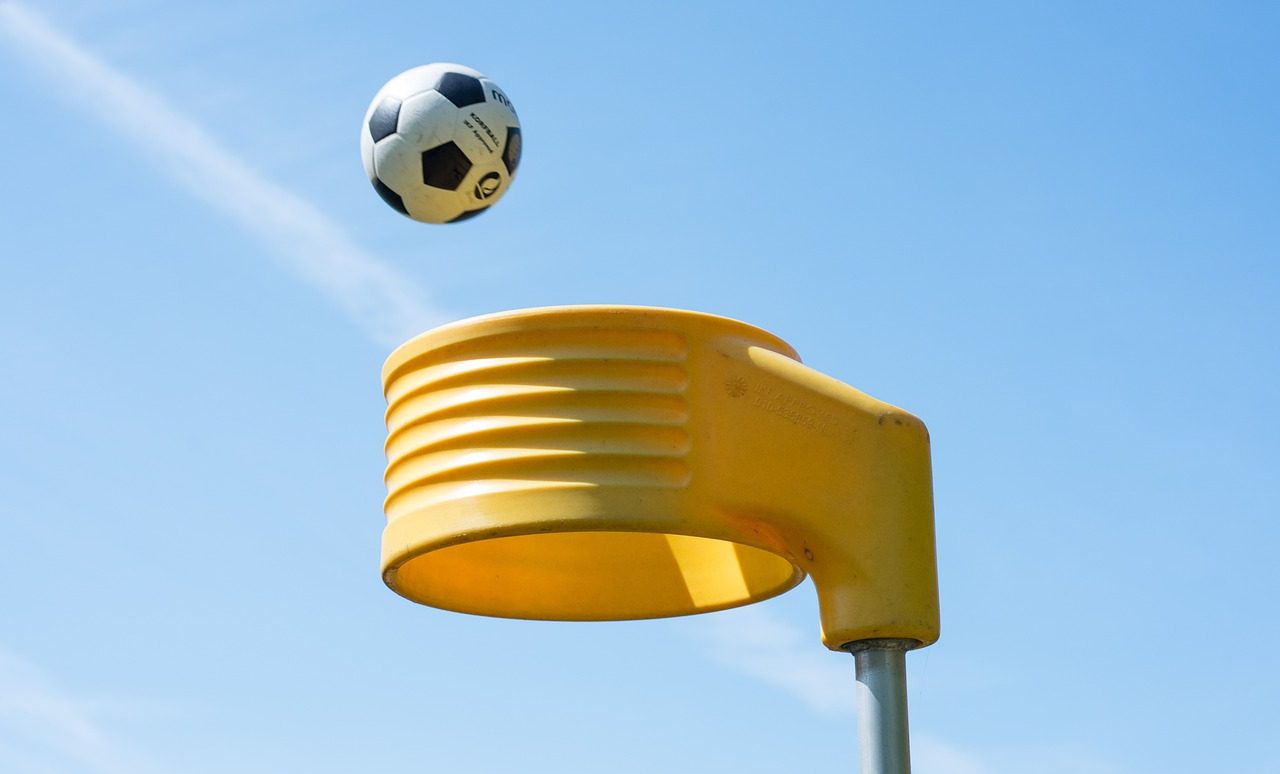 A yellow korfball korf on a steel post, with a korfball ball entering the korf